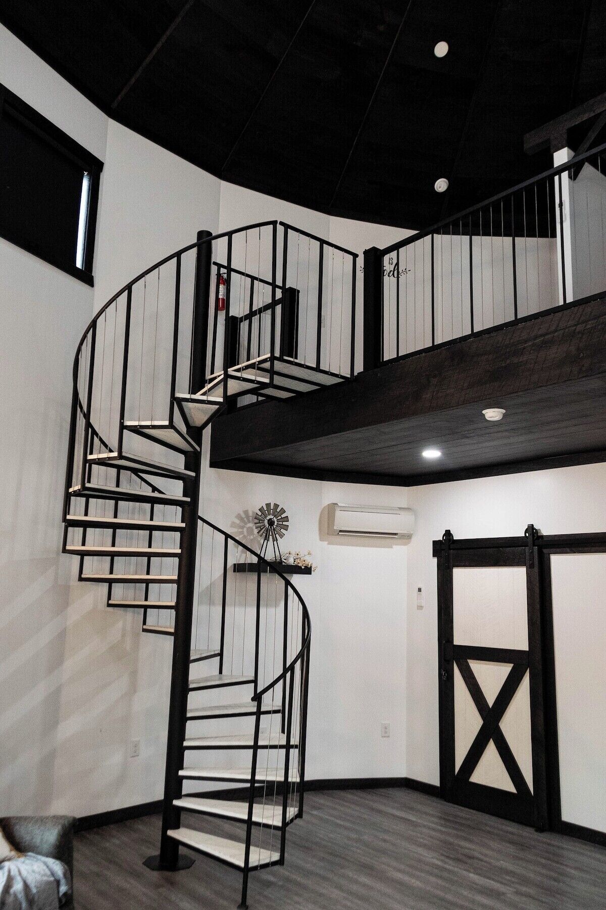 A spiral staircase with a black railing, a windmill decoration, and a barn-style door.