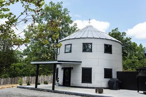 A white, circular building with a metal roof, a black door, and a small porch area. - Grain Bin - Unique Stay (Peebles)