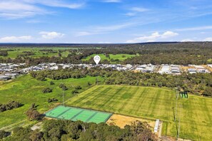 An aerial view of a residential area with houses, green fields, and a sports court.
