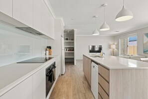 A modern kitchen with white cabinetry, a central island, pendant lighting, and a view to the outside. - Modern Getaway in Dunsborough (Dunsborough)