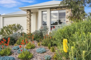 A modern house with a brick facade, large windows, and a well-maintained garden with various plants and flowers. - Modern Getaway in Dunsborough (Dunsborough)
