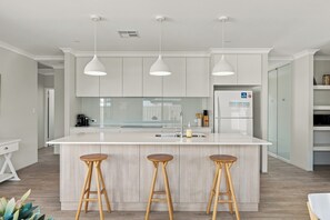 A modern kitchen with a central island, bar stools, pendant lighting, and a built-in refrigerator.