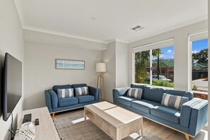 A modern living room with two sofas, a coffee table, a TV, and a large window with a view of a construction site. - Modern Getaway in Dunsborough (Dunsborough)