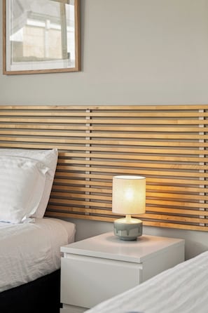A neatly made bed with white bedding, a bedside table with a lamp, and a wooden slatted headboard. - Modern Getaway in Dunsborough (Dunsborough)