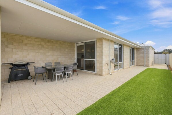 A covered patio area with a barbecue grill, outdoor seating, and a well-maintained lawn. - Modern Getaway in Dunsborough (Dunsborough)