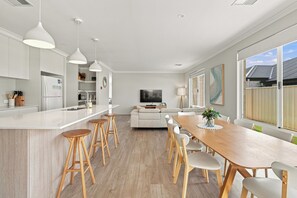 A modern kitchen with a central island, bar stools, and a dining area with a wooden table and chairs. - Modern Getaway in Dunsborough (Dunsborough)