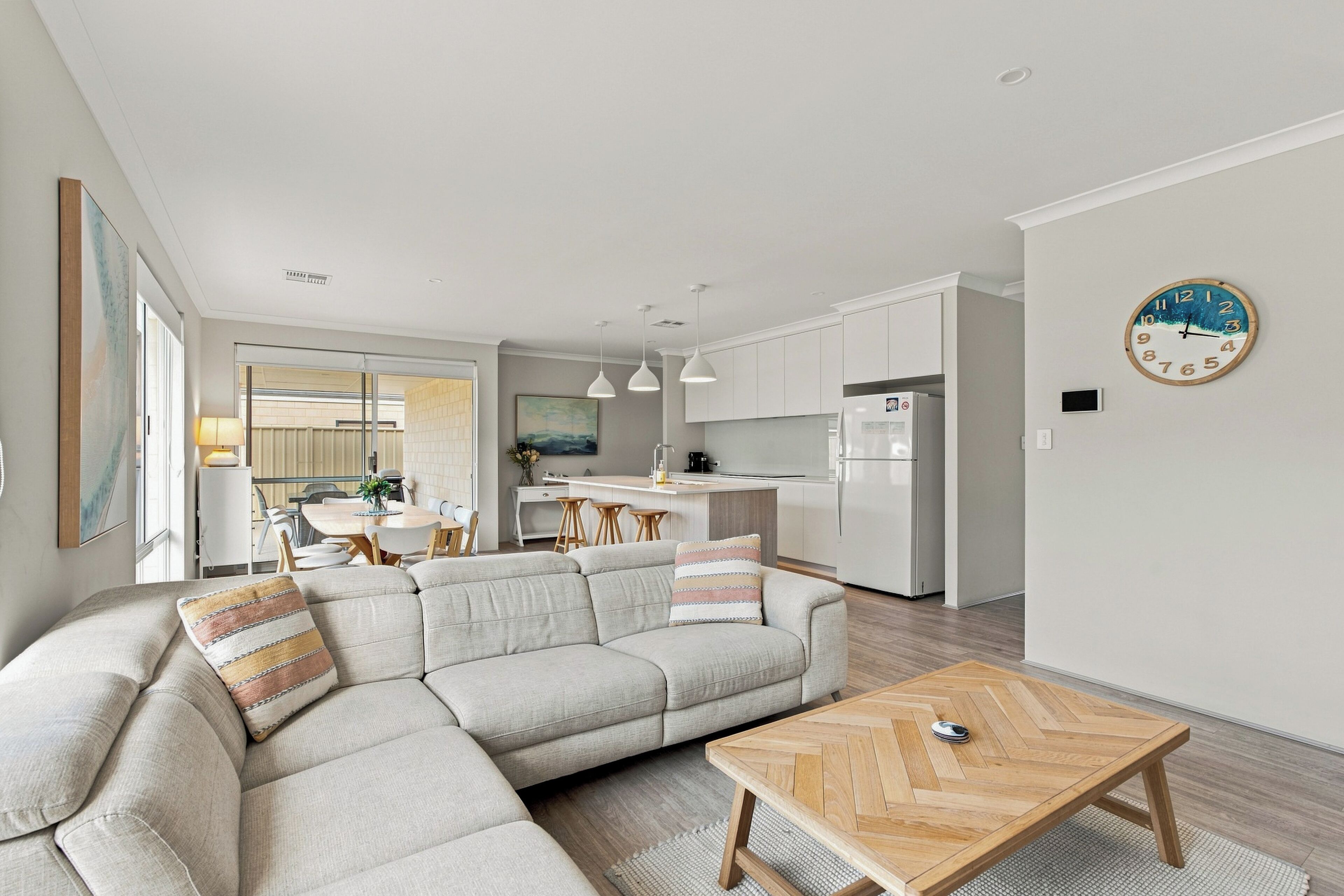 A modern living room with a sectional sofa, a herringbone coffee table, and a kitchen in the background.