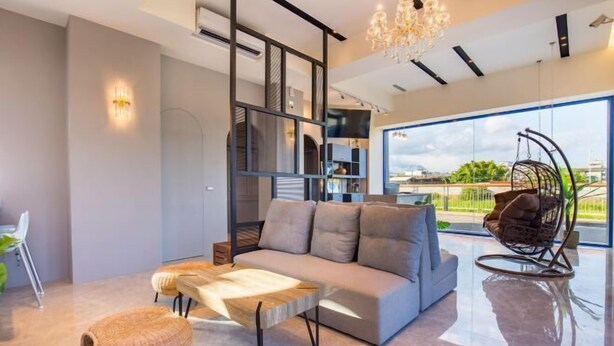 Un salon moderne comprenant un canapé, une table basse, un fauteuil suspendu et une grande fenêtre donnant sur l’extérieur.