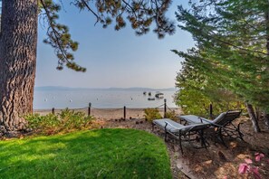 A lakeside view with a grassy area, two lounge chairs, and a fence. - Lakefront Lake Tahoe Retreat with Fire Pit (Homewood)