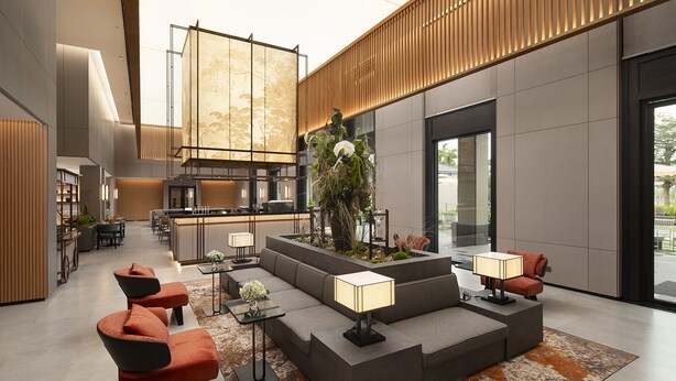 Eine moderne Lobby mit einer zentralen Sitzecke, einem Empfangstresen und einem großen Fenster mit Blick ins Freie.