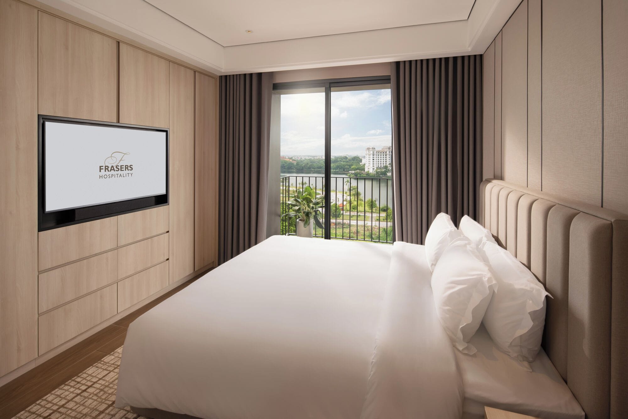 A hotel room with a large bed, a television mounted on the wall, and a view of a cityscape through the window.