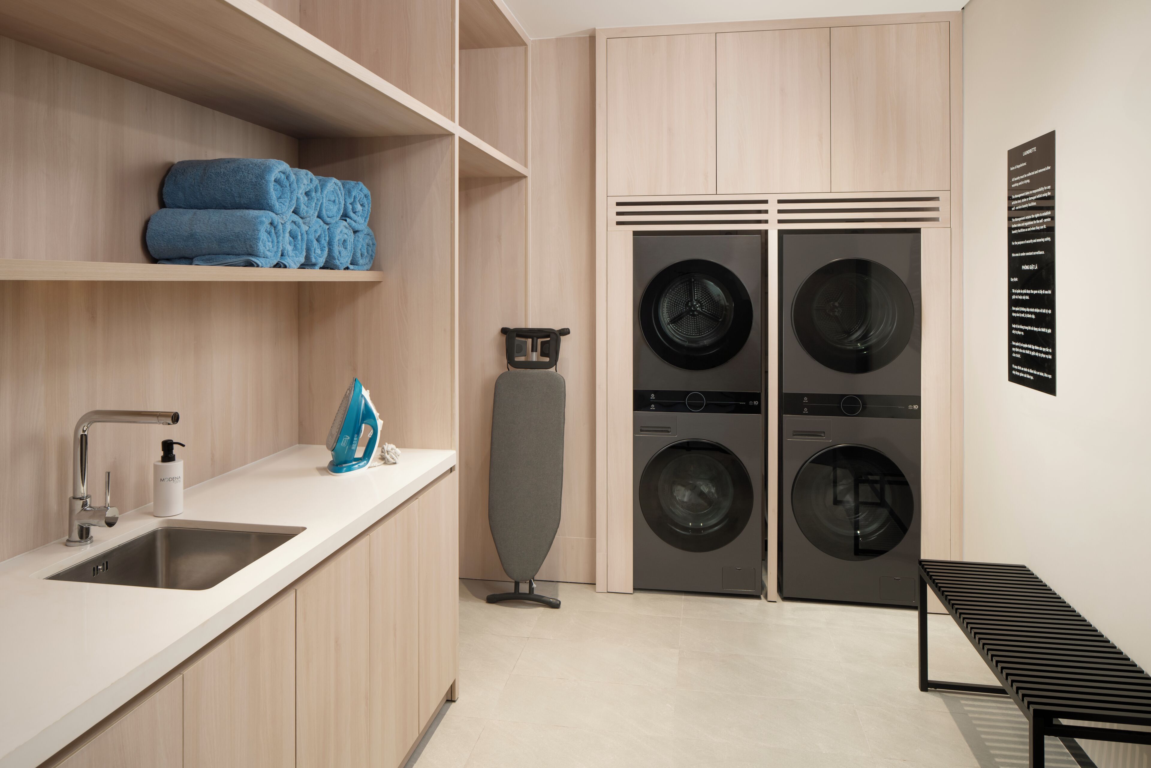 A modern laundry room with a sink, stacked towels, a drying rack, and two front-loading washing machines.
