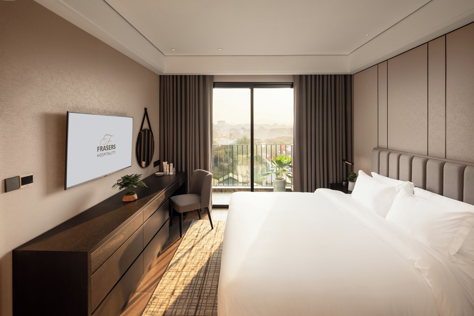 Et moderne hotelværelse med en stor seng, et skrivebord med en computer, et fjernsyn ophængt på væggen og en balkon med udsigt over byen.