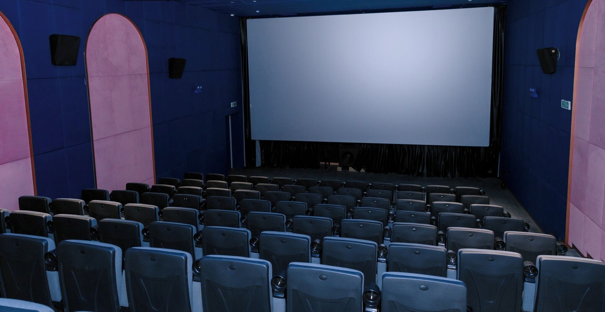 An empty movie theater with rows of seats, a large screen, and a stage.