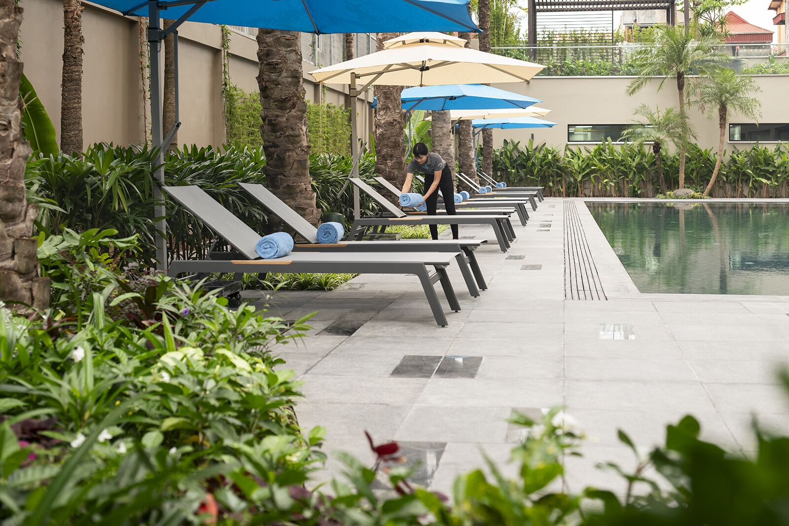 A poolside area with lounge chairs and umbrellas, surrounded by greenery and a stone wall.