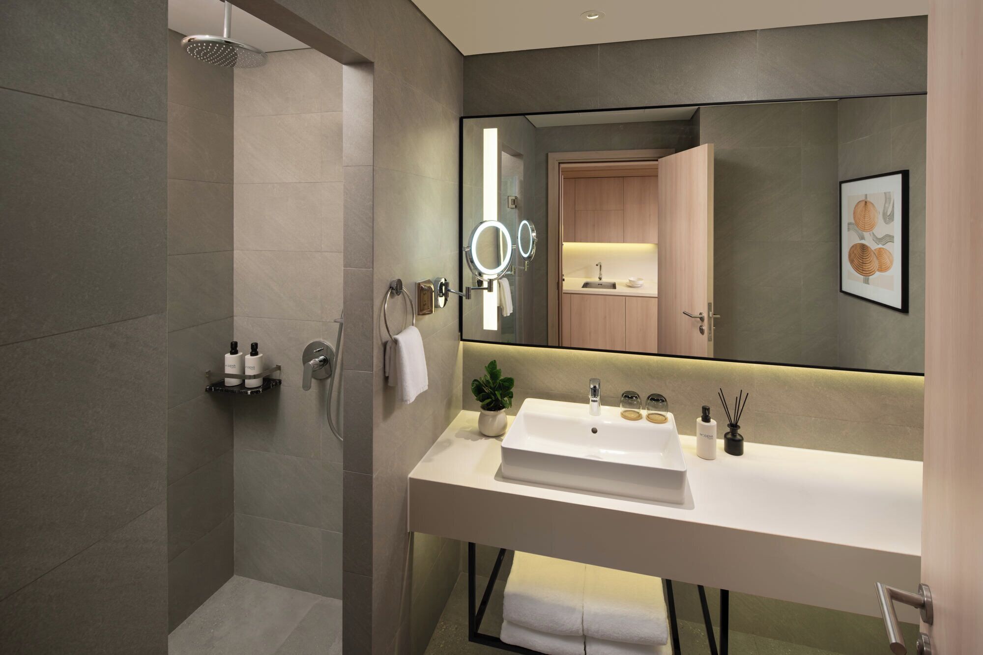 A modern bathroom with a large mirror, a shower, and a white sink with a countertop.