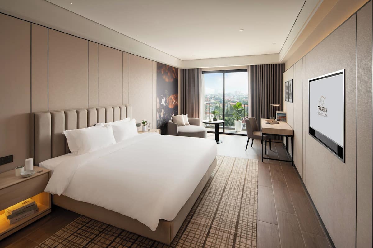 A modern hotel room with a large bed, a desk, and a view of the city.