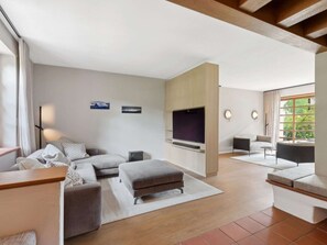 A modern living room with a sectional sofa, a flat-screen TV, and a dining area with a table and chairs.