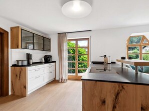 Une cuisine moderne avec des meubles en bois, un plan de travail noir et une grande fenêtre donnant sur un paysage verdoyant.