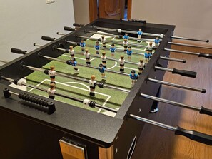 A foosball table with a dark surface and multiple rods, featuring player figures in blue and white uniforms.