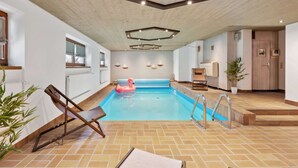 Ein beheiztes Hallenbad mit Holzbalkendecke, gefliestem Boden und blauem Wasser.