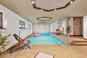 Una piscina interior con techo de madera, suelo de baldosas y agua azul.