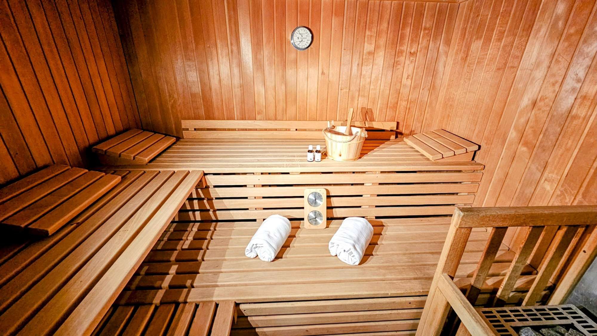 Una sauna con bancos de madera, un cubo de madera y dos toallas.
