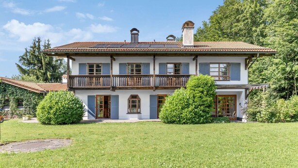 Ein zweistöckiges Haus mit Balkon, gepflegtem Rasen und blauem Himmel.