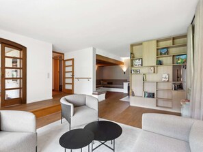 Un salon moderne avec un canapé, deux tables noires et une bibliothèque remplie de livres et de jeux.