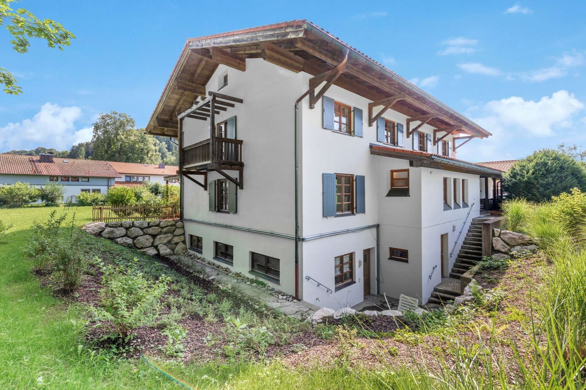 Una casa a due piani con fondamenta in pietra, balcone in legno e una scala che conduce al piano superiore.