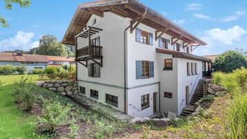 Una casa a due piani con fondamenta in pietra, balcone in legno e una scala che conduce al piano superiore.