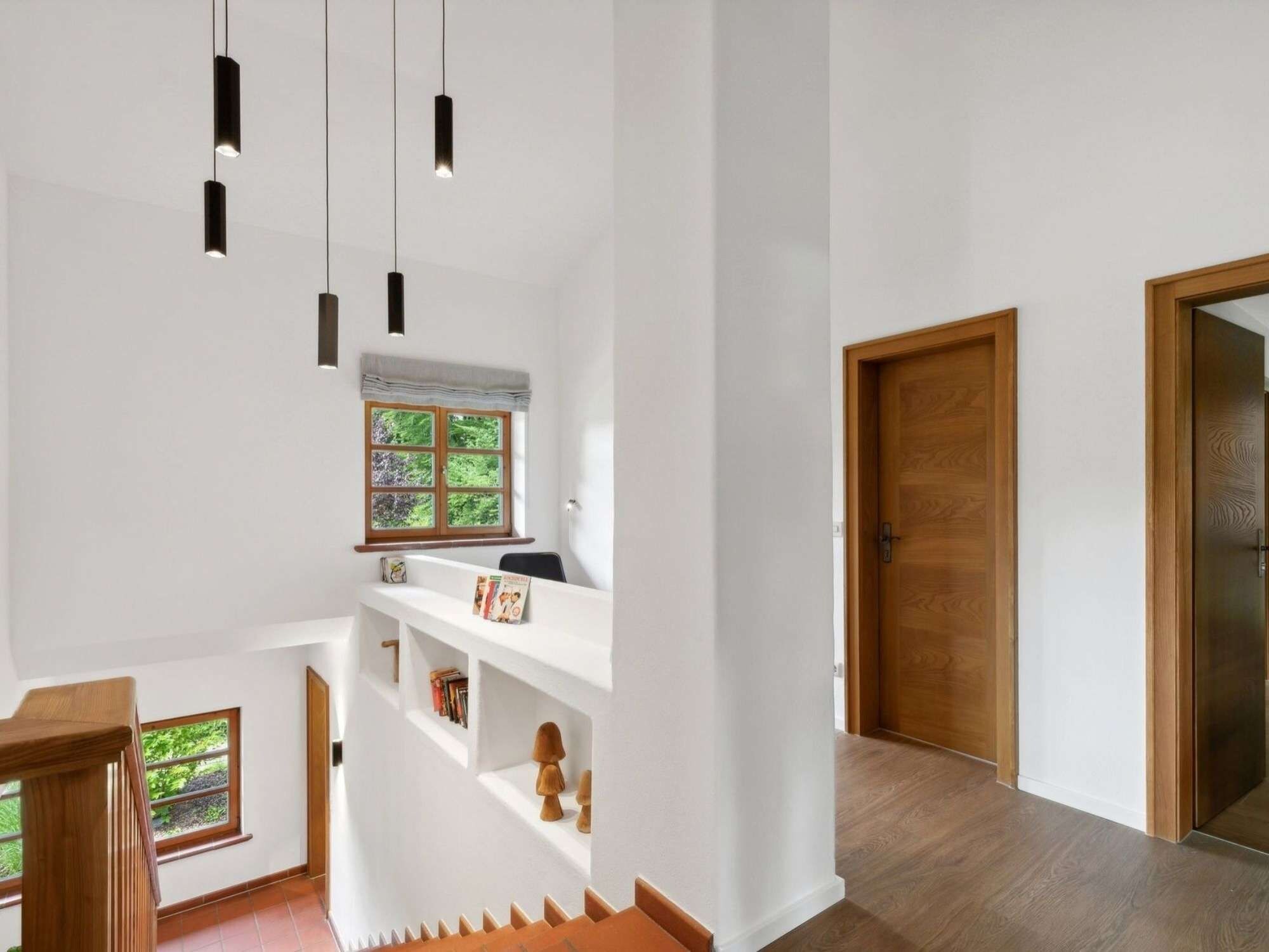 A modern interior with a staircase, a wooden door, and pendant lighting.