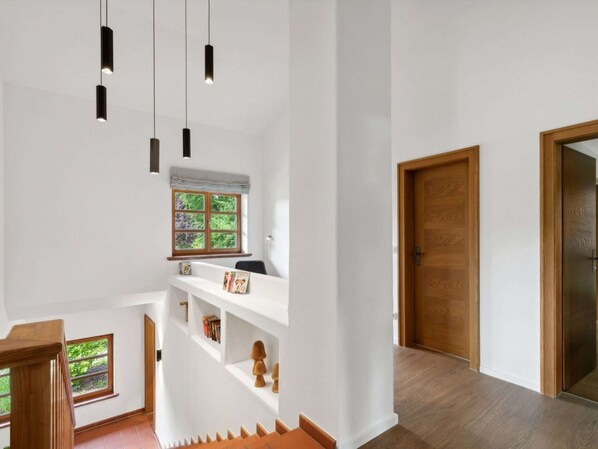 A modern interior with a staircase, a wooden door, and pendant lighting.