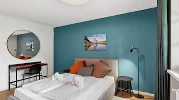 A modern bedroom with a bed, a desk, a chair, a round mirror, a painting, and a floor lamp.