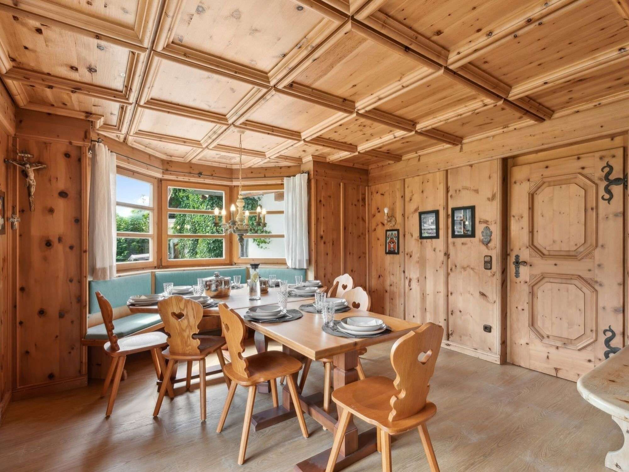 A wooden dining room with a long table set for four, surrounded by wooden chairs with heart-shaped cutouts.