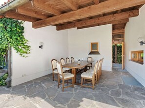 A stone-floored patio with a wooden table and chairs, a hanging plant, and a small window.