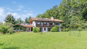 Ein zweistöckiges Haus mit Balkon, umgeben von einem gepflegten Rasen und Bäumen.