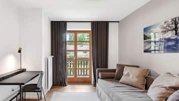 Ein modernes Wohnzimmer mit einer Couch, einem Schreibtisch und einem Sessel. Es gibt ein großes Fenster mit Vorhängen, eine Heizung und ein Bild an der Wand.