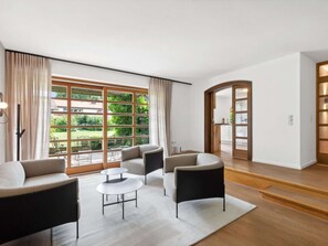 Un salon moderne avec une grande fenêtre, un ensemble de canapés, une table basse et une bibliothèque.