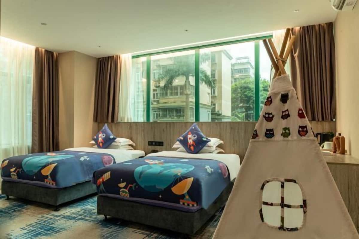Habitación de hotel con dos camas, un ventanal grande, una tienda tipi y vistas a edificios.