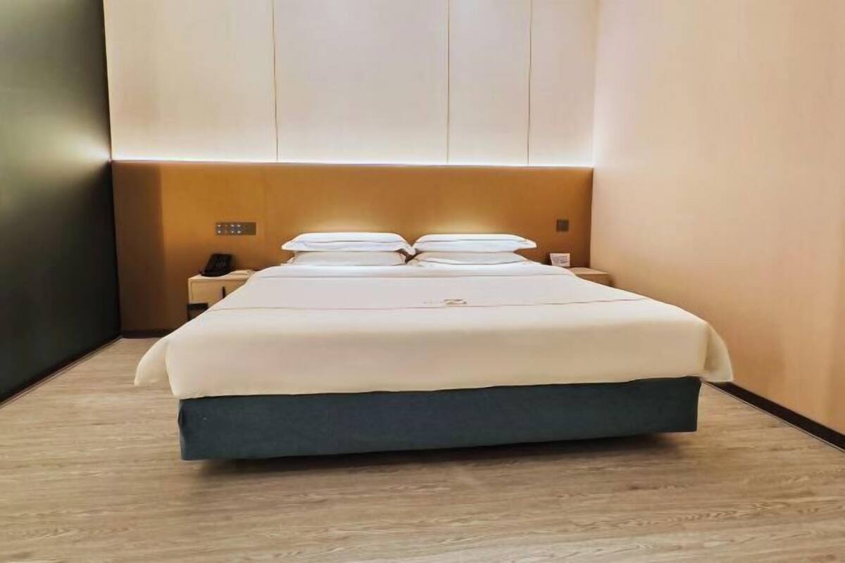 A modern hotel room with a large bed, bedside tables, and a wall-mounted control panel.
