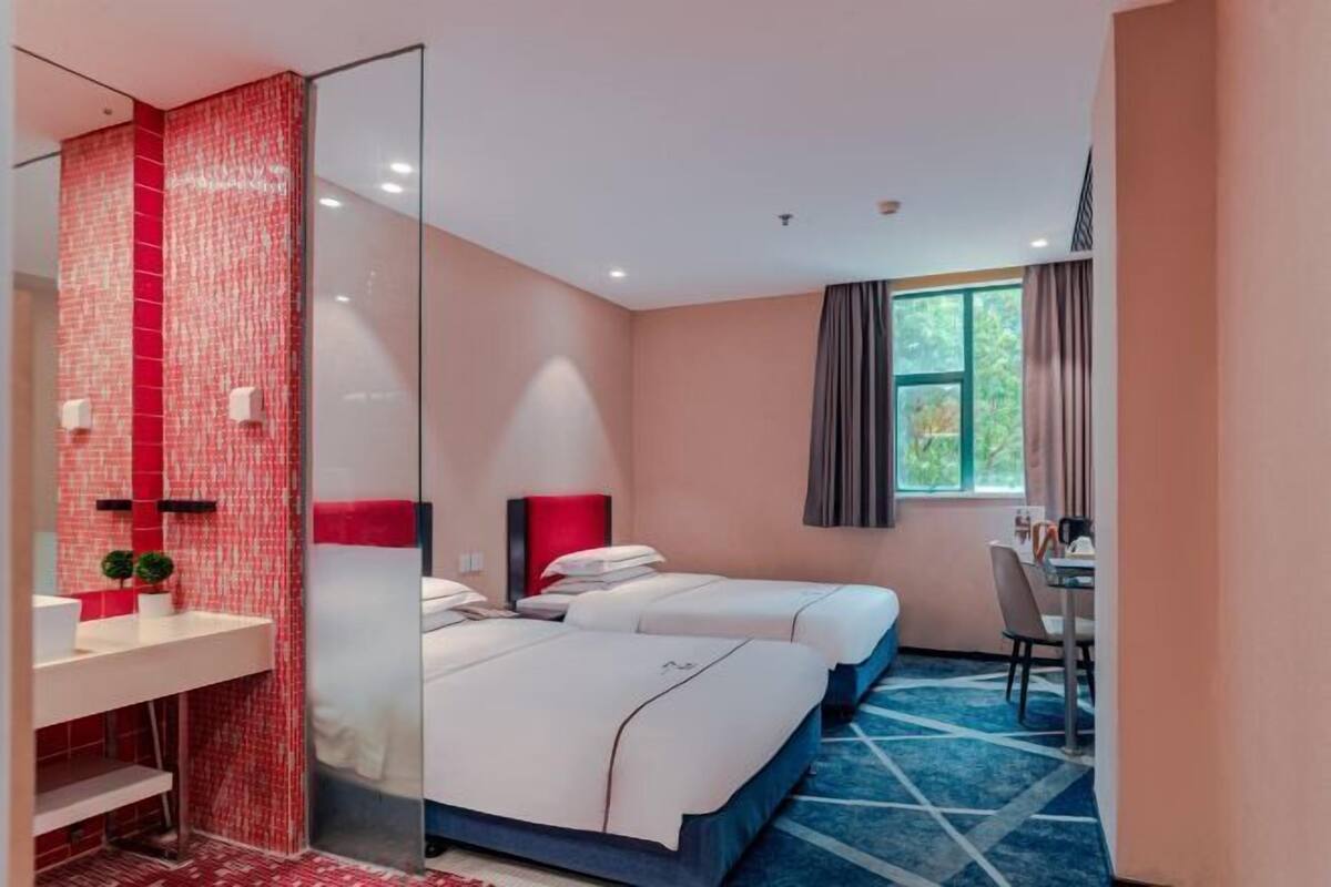 Habitación de hotel con dos camas, un baño con ducha de azulejos rojos, un escritorio y una ventana con cortinas.