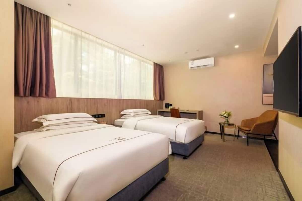 Habitación de hotel con dos camas, un escritorio, una silla y un equipo de aire acondicionado.