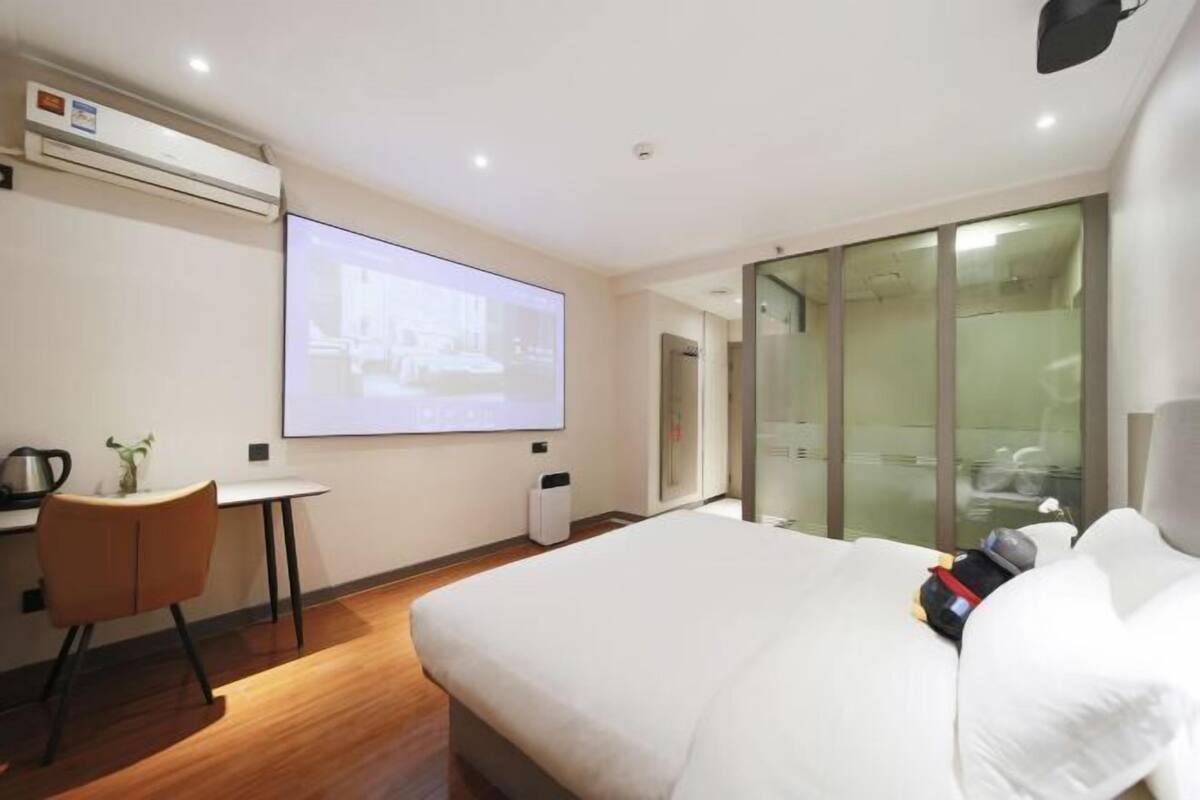 Ett hotellrum med en säng, ett skrivbord med en stol, en projektorduk och en glasvägg.