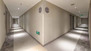 A long, narrow hotel corridor with a patterned carpet, recessed ceiling lights, and a green exit sign on the wall. - Homeinn Hotel (Ningbo Tianyi Square Center) (Ningbo)