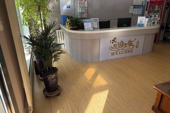 A reception desk with a 'WELCOME' sign, a potted plant, and a window with natural light. - Haojin Business Hotel (Erenhot)
