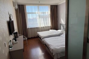 Habitación de hotel con dos camas, un escritorio pequeño con una silla, un radiador y una ventana con cortinas.