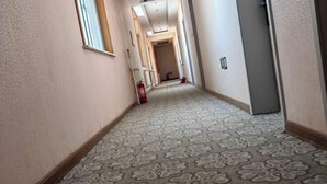 A carpeted hallway with a patterned floor, a fire extinguisher, and a door on the right. - Haojin Business Hotel (Erenhot)