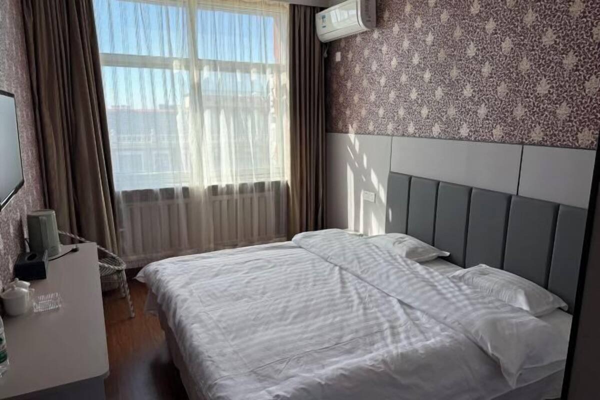 Habitación de hotel con cama, escritorio con lámpara, silla y ventana con cortinas.