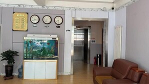 A lobby with a fish tank, clocks, and a couch. - Haojin Business Hotel (Erenhot)